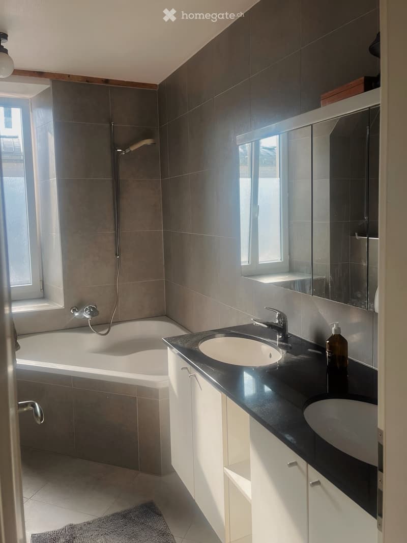 Modern bathroom with a bathtub, double sink, large mirror, and sleek black countertop.
