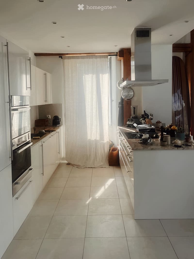 Modern kitchen with white cabinets, stainless steel appliances, and a large island. Features include a built-in oven, a blender, and various kitchen utensils on the counter.