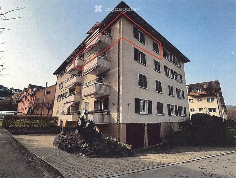 Multi-story residential building with multiple balconies and windows, surrounded by greenery and neighboring structures.