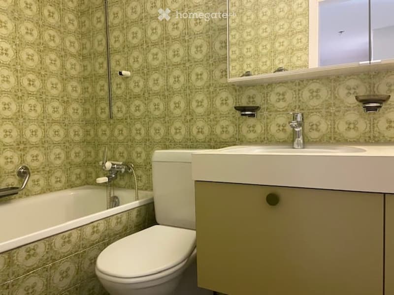 Bathroom with green patterned tiles, a bathtub, toilet, sink, and a mirror above the sink.
