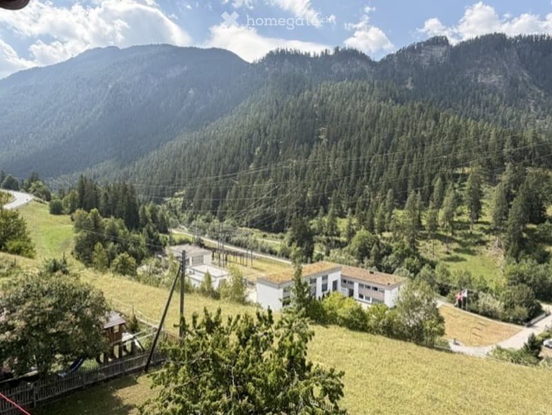 Panoramic view of a lush green valley with mountains in the background, featuring scattered houses and a winding road.