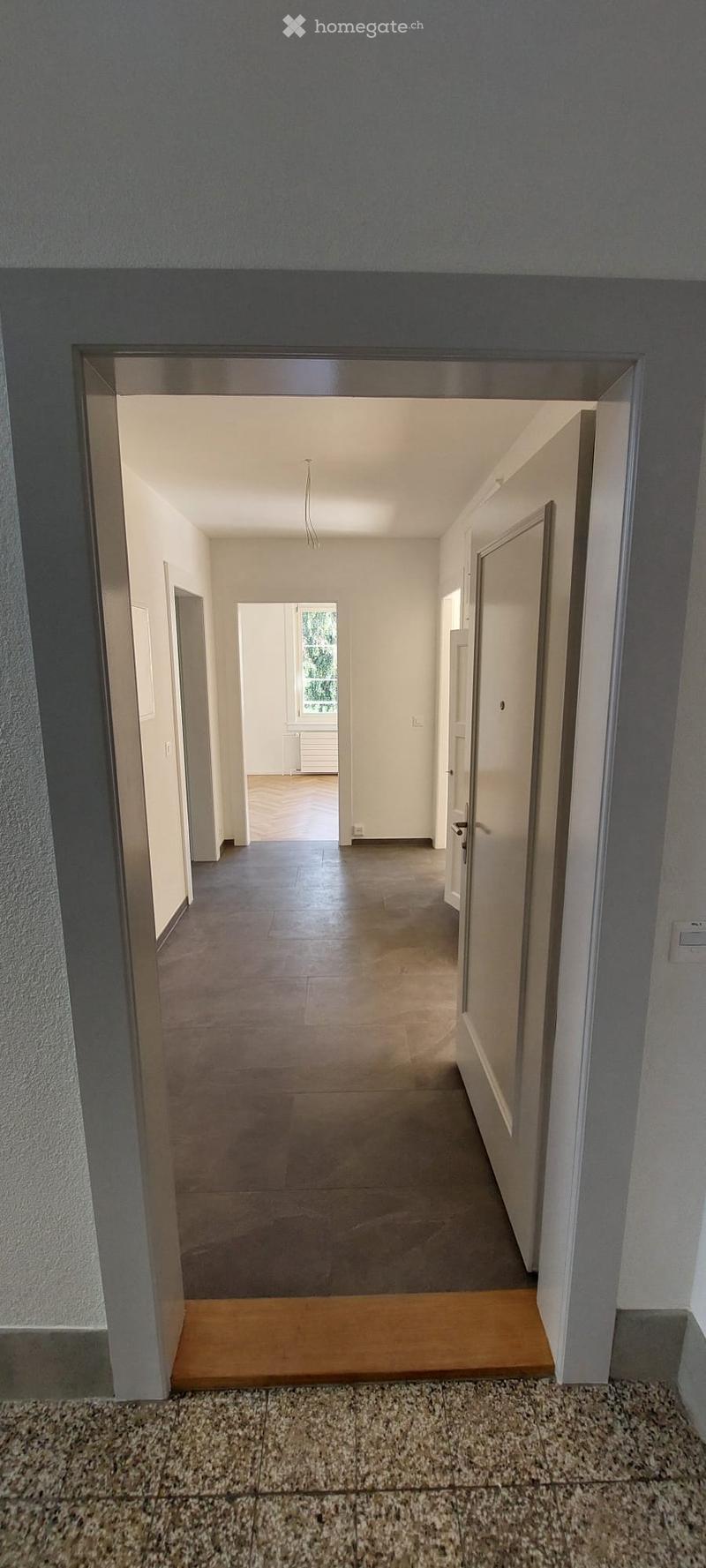 Empty hallway with tiled floor, white walls, and multiple doors leading to other rooms.