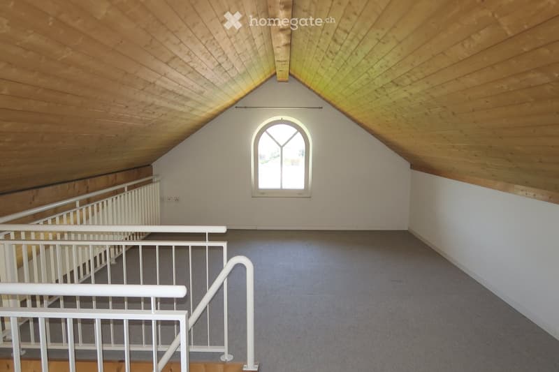 An empty attic room with wooden ceiling and floor, a white handrail, and an arch window.