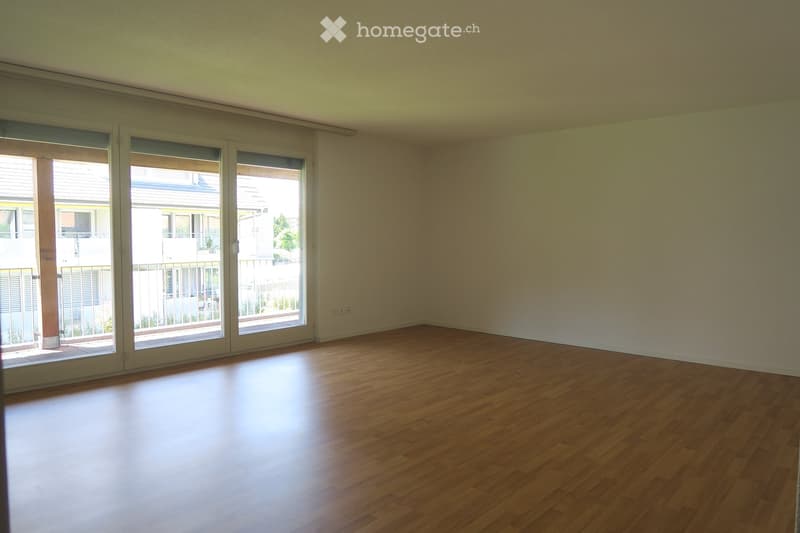 spacious, modern room with wooden floor, large glass doors leading to a balcony, white walls, view of the outside