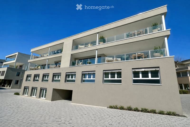Modern multi-story building with large windows and balconies, featuring contemporary design and clean lines.