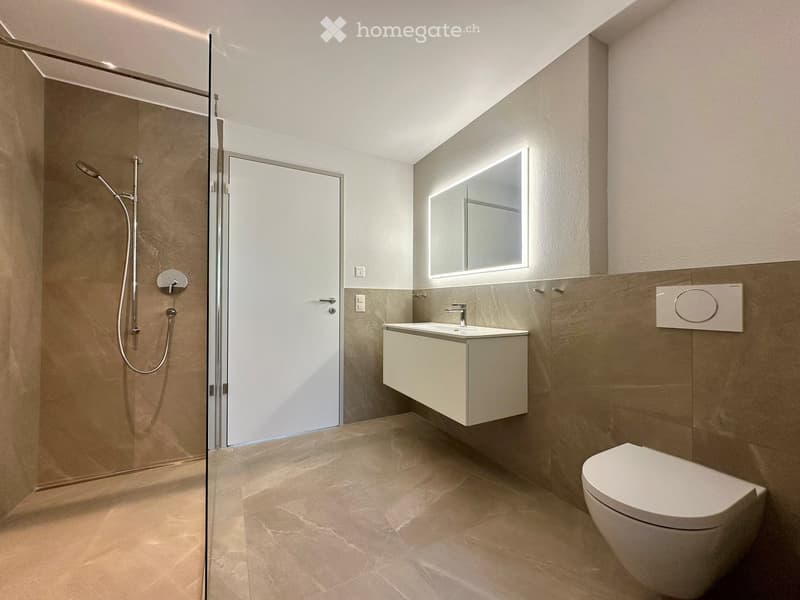 Modern bathroom with shower, sink, and toilet. Tiled floor and walls, glass door for shower, white vanity with sink, and mirror.