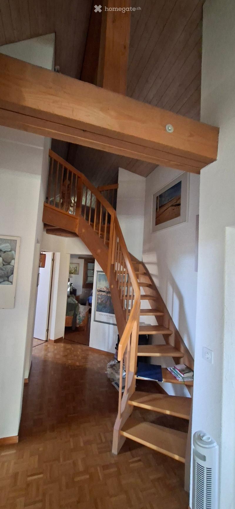 Spacious hallway with wooden staircase leading to an upper level, wooden floors, white walls, and framed artwork on the walls.