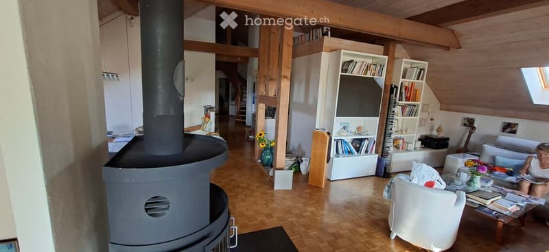 Cozy living room with wooden floors, exposed wooden beams, a large fireplace, a sofa, coffee table, bookshelf, and a guitar in the corner.