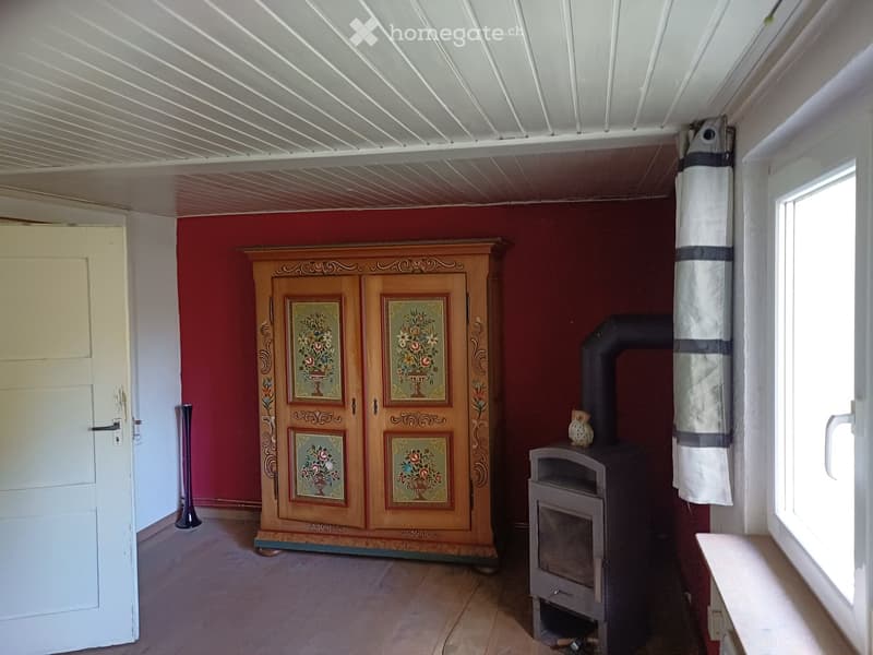 Room with red walls, wooden floor, a large wooden cabinet with floral designs, a wood stove, and a decorative owl on top of the stove.