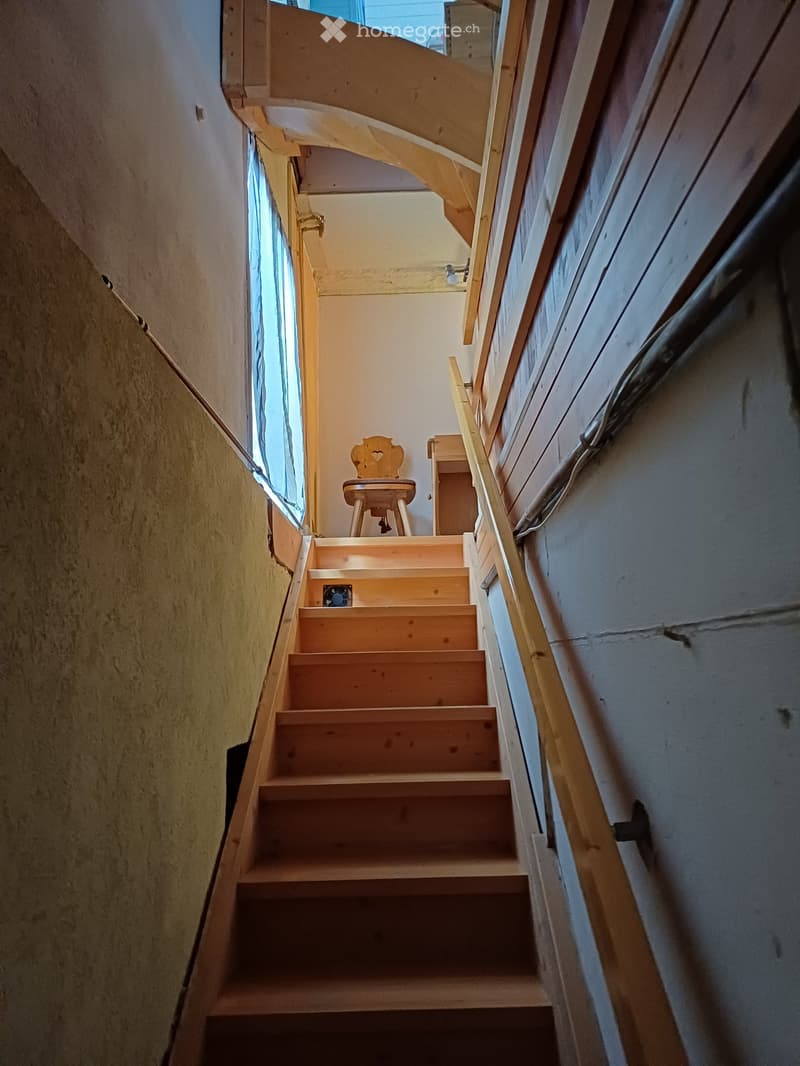 Wooden staircase with a handrail, small wooden chair, and window with blue curtains at the top of the stairs.