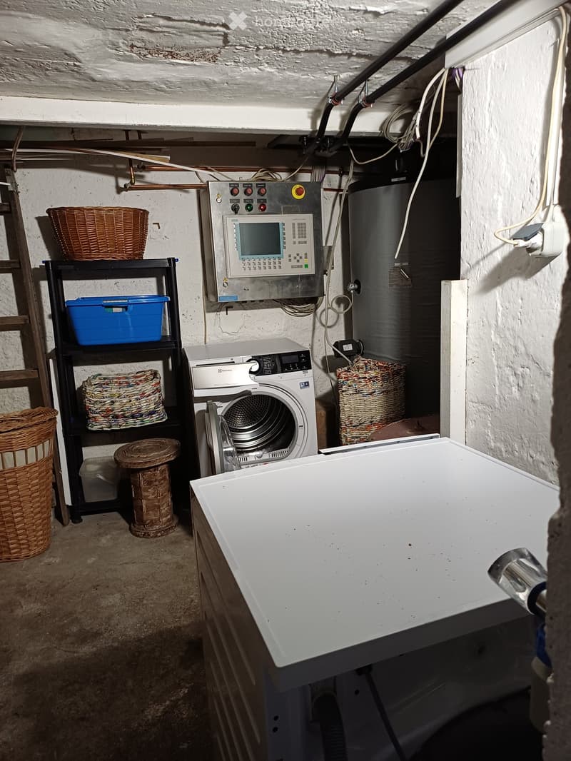 Utility room with a washing machine, dishwasher, control panel, wicker baskets, and a small stool.
