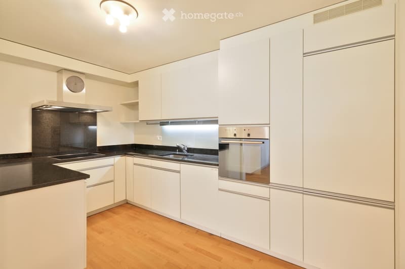 Modern kitchen with white cabinets, black countertops, stainless steel appliances, and wooden flooring.