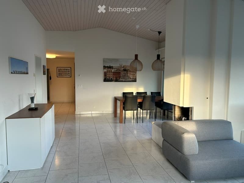 Open-plan living and dining area with a grey sofa, wooden dining table with chairs, white cabinet, and pendant lights.