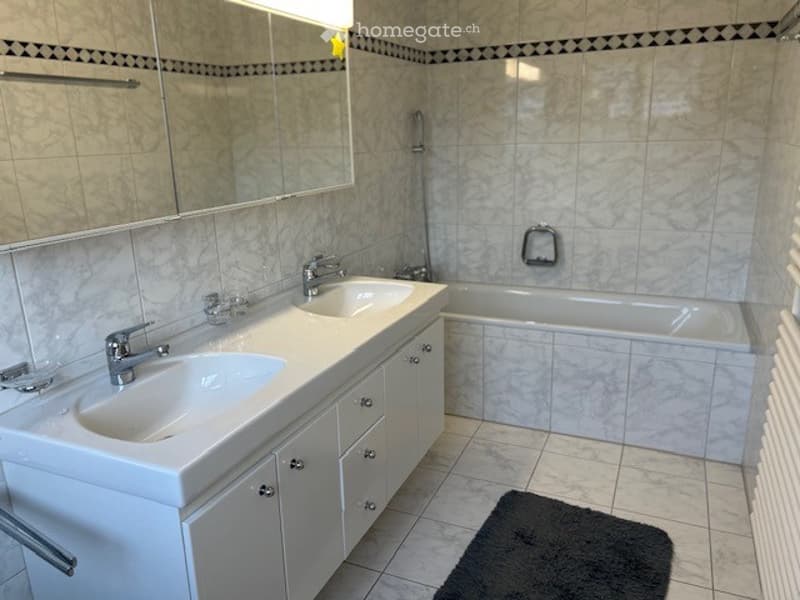 Modern bathroom with double sink vanity, bathtub, large mirror, and tiled walls.