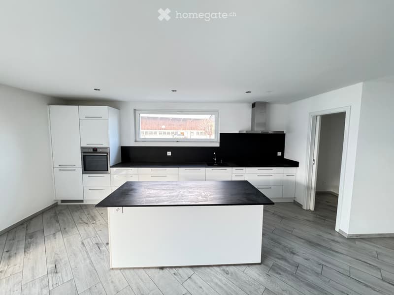 Modern kitchen with white cabinets, black countertops, a central island, and a large window offering a view.