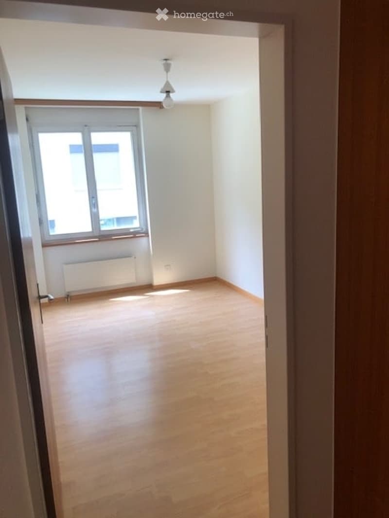 Empty room with wooden flooring, white walls, and a single window with a radiator below it. The room is unfurnished and has a simple, clean design.
