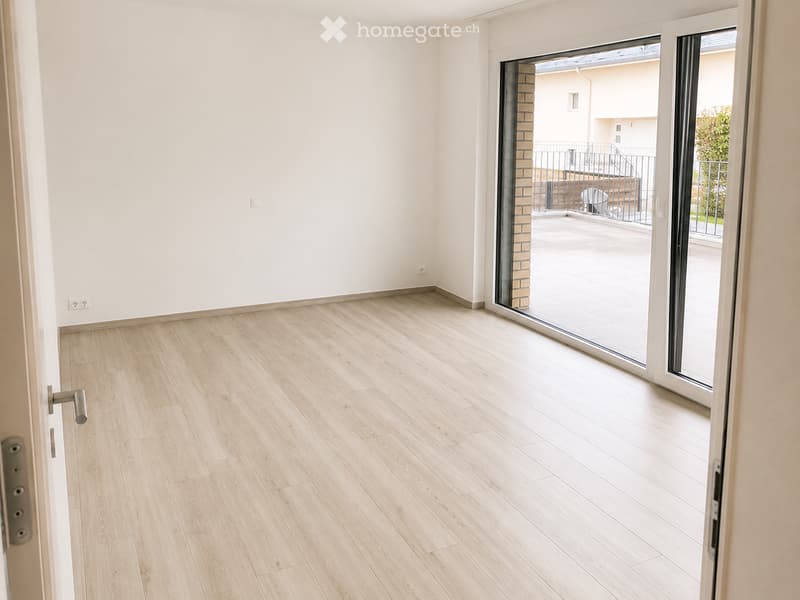 Empty room with light wooden flooring, white walls, and a large sliding glass door leading to a balcony area.