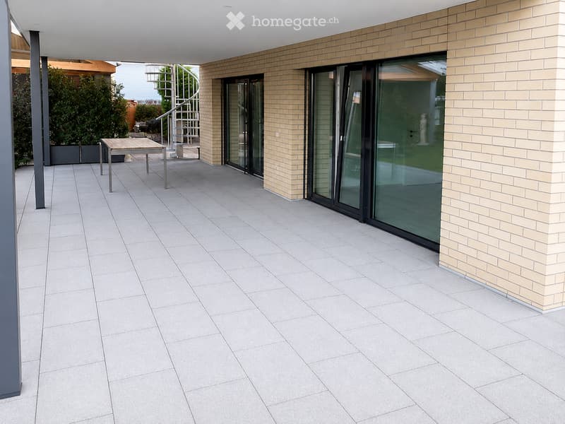 Modern balcony with light grey tiled floor, sliding glass doors, and a small table with chairs.