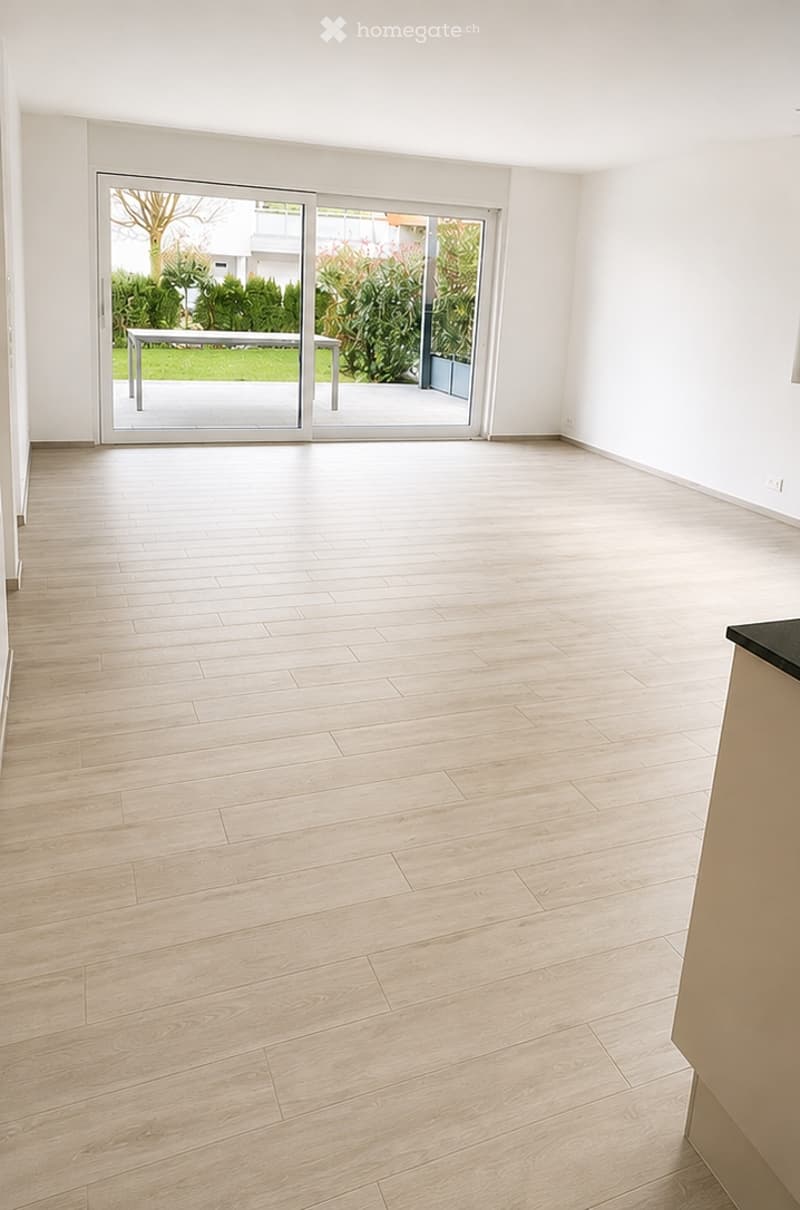 Empty room with light wooden flooring, white walls, and large sliding glass doors leading to a garden area.