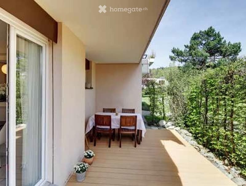 Balcony with wooden flooring, a small dining area with a table and chairs, and potted plants. Offers a scenic view of greenery and trees.