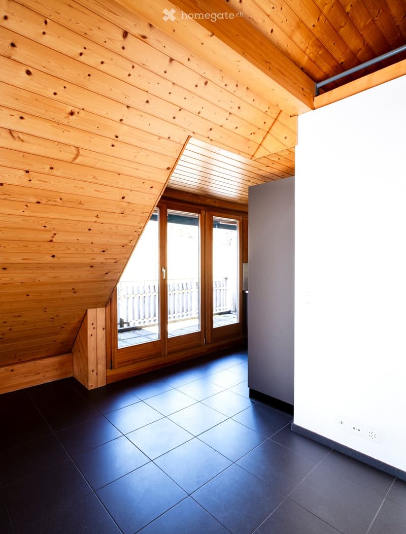 An empty attic space with wooden walls and ceiling, dark tiled floor, and large sliding glass doors leading to an outdoor area.