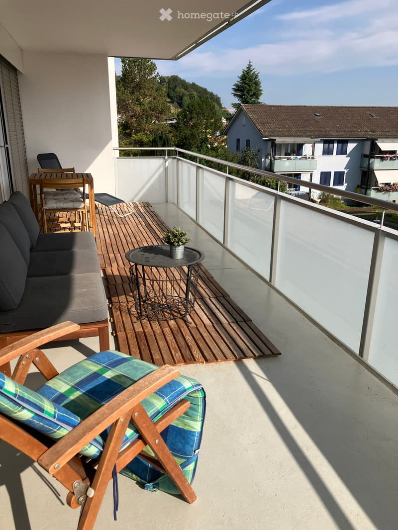Balcony with wooden decking, sofa, chair, small table with a potted plant, and a view of the surrounding area.