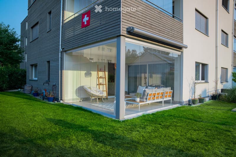 Modern two-story house with large glass walls, balcony, and well-maintained lawn.