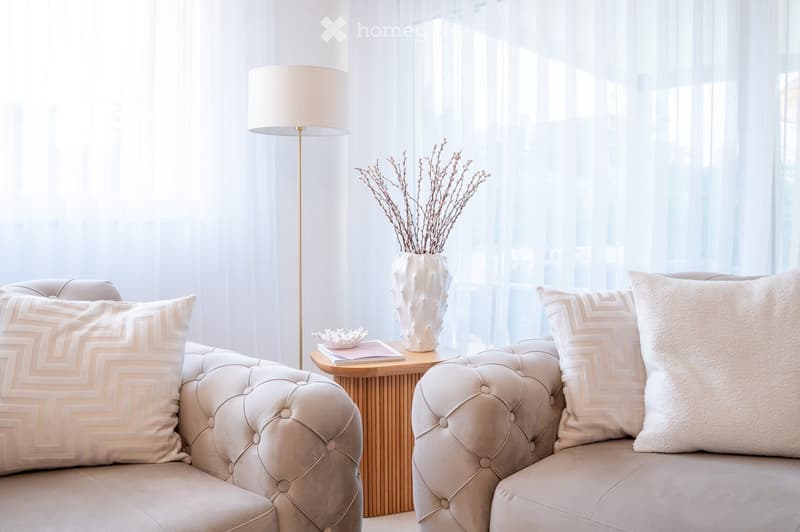 Modern living room with a light-colored sofa, decorative pillows, a small wooden side table, a vase with dried branches, and a floor lamp.