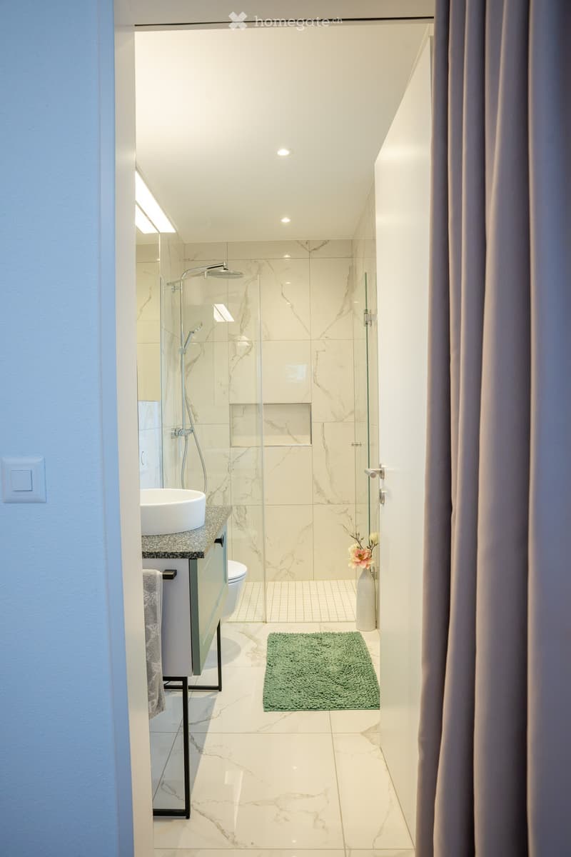 Modern bathroom with marble tiles, glass shower enclosure, sink, toilet, and decorative vase with flowers.