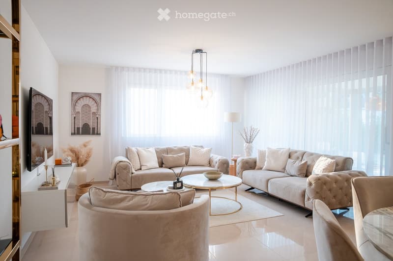 Modern living room with large windows, white walls, beige sofa, coffee tables, and decorative items.