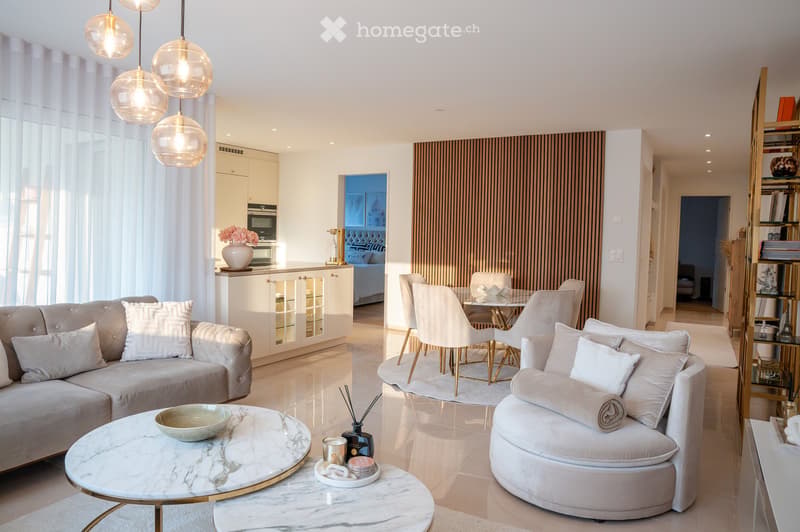 Modern living room with a white sofa, round marble coffee table, white dining table with chairs, and a view of a bedroom through an open doorway.