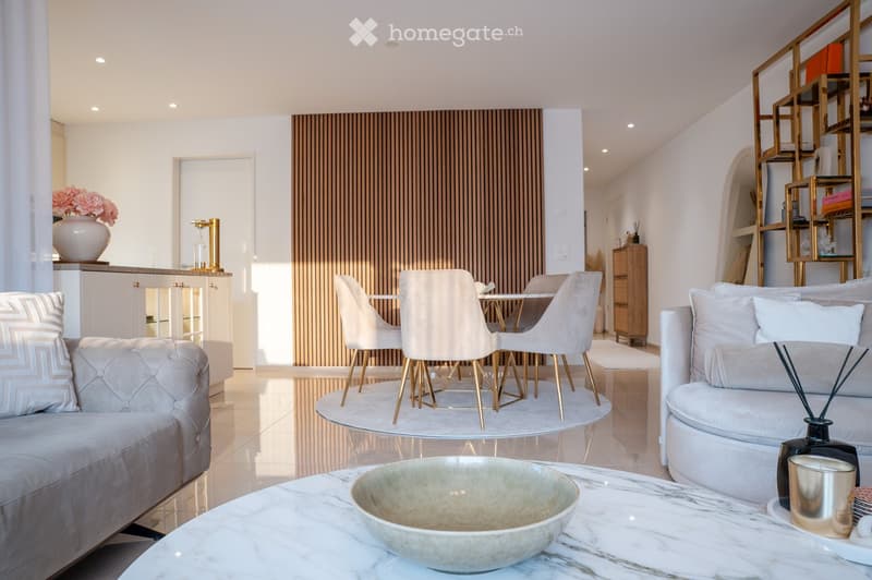 Modern living room with a white sofa, coffee table, dining area with chairs and table, decorative vase, and shelves.