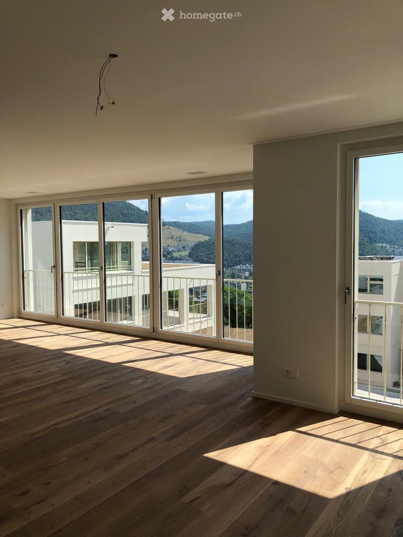 Empty room with wooden flooring, large sliding glass doors leading to a balcony, and a scenic mountain view.