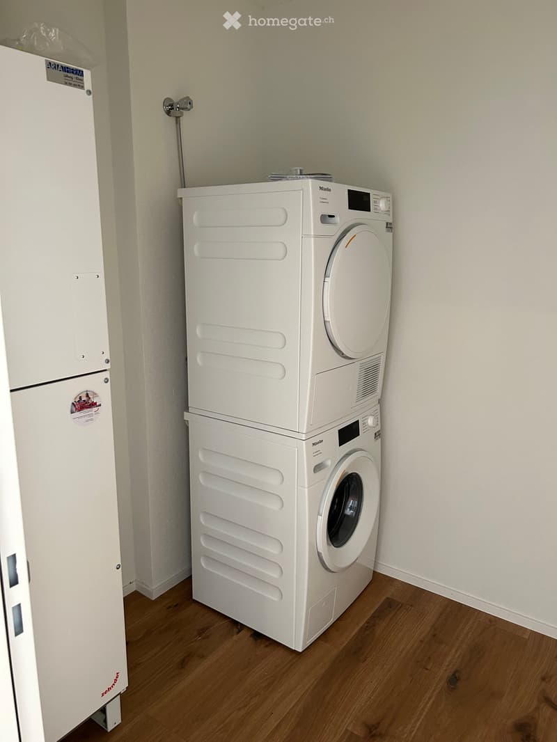 A small bathroom with a wooden floor, white walls, and a stacked washing machine and dryer unit.