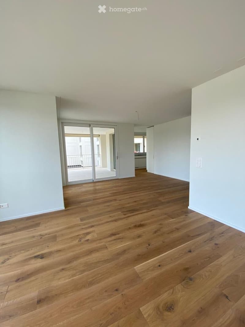 Completely empty room with wooden flooring and large sliding glass doors leading to a balcony.
