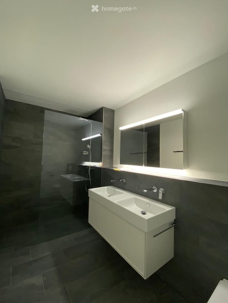 Modern bathroom with a double sink, large mirror with built-in lighting, and a separate bathtub area.