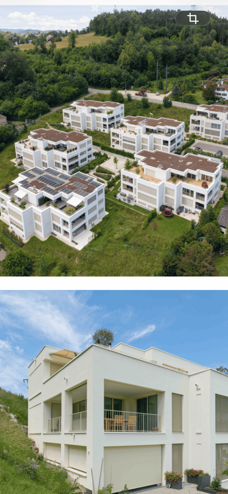 Aerial view of a modern residential complex with multiple white buildings, solar panels, balconies, and landscaped gardens.