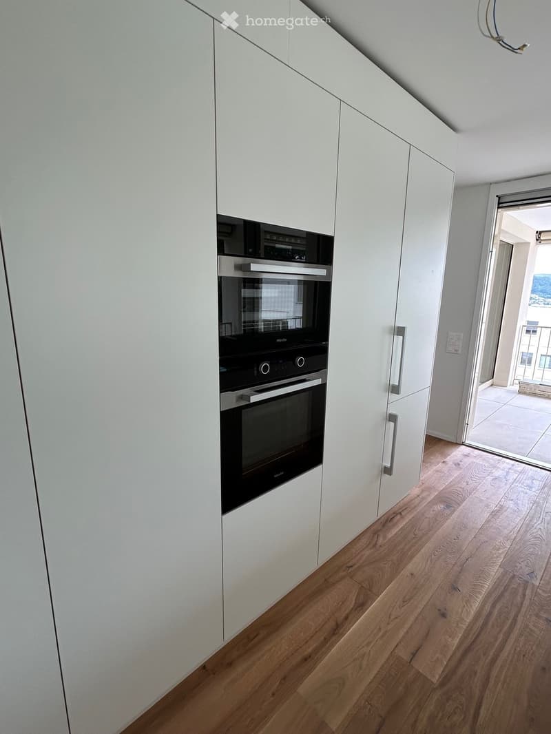 Modern kitchen with white cabinets, wooden flooring, and built-in oven.