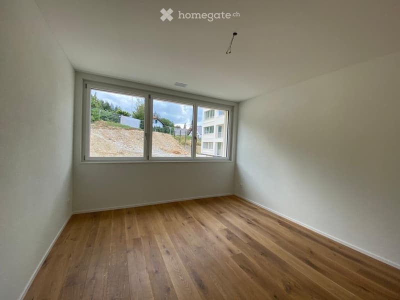 Empty room with wooden flooring and large windows offering a view of the outside area.