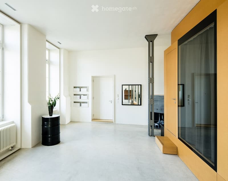 Minimalist, unfurnished room with white walls, concrete floor, large windows, and a few decorative elements like a vase with flowers and a small shelf.