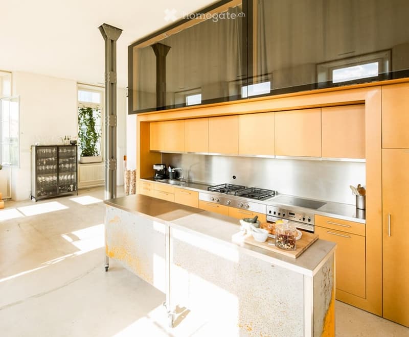 Modern kitchen with light wood cabinets, stainless steel appliances, island, and various kitchen items on the counter.