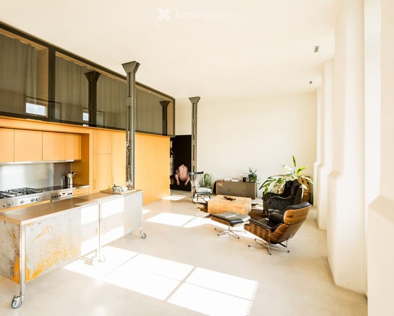 Open-plan kitchen and living area with modern design, featuring a kitchen island, stove, cabinets, a chair, a coffee table, a stool, plants, and a sofa.