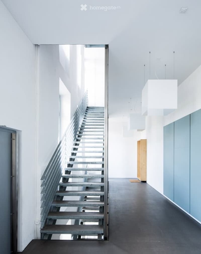 Modern, minimalist hallway with a sleek metal staircase leading upwards, white walls, and contemporary lighting fixtures.