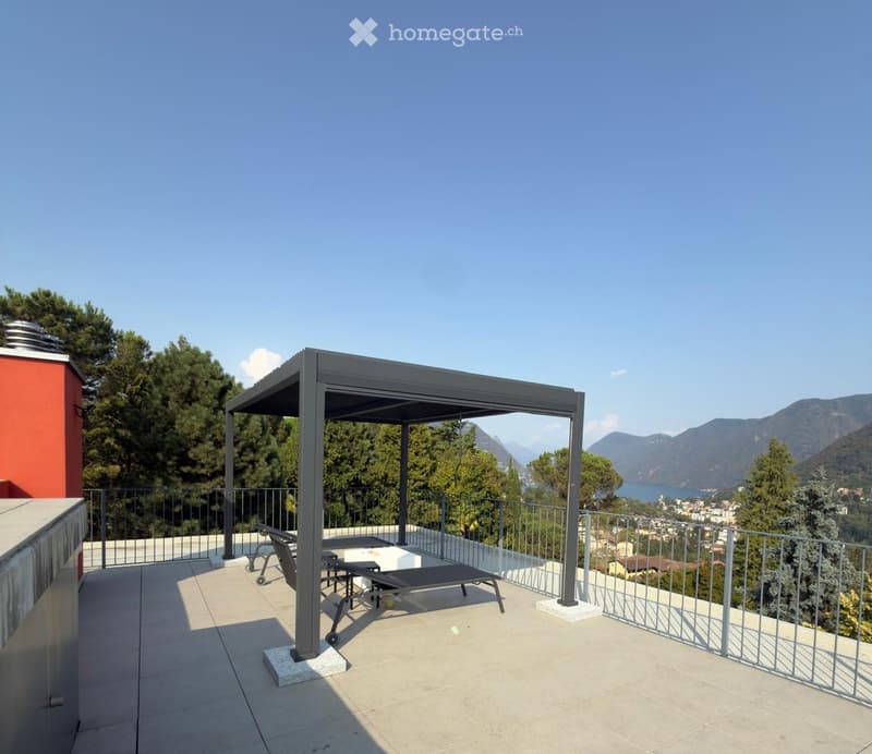 A modern balcony with a metal pergola, a table, and chairs, overlooking a scenic lake and mountains.