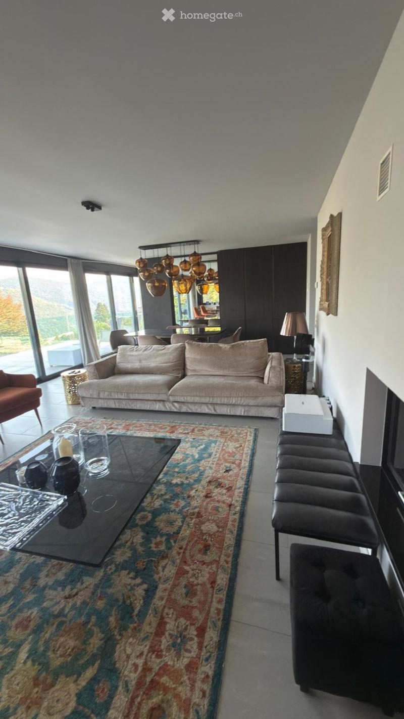 Modern living room with large windows, a beige sofa, a black coffee table, a patterned rug, and a bench along the wall.