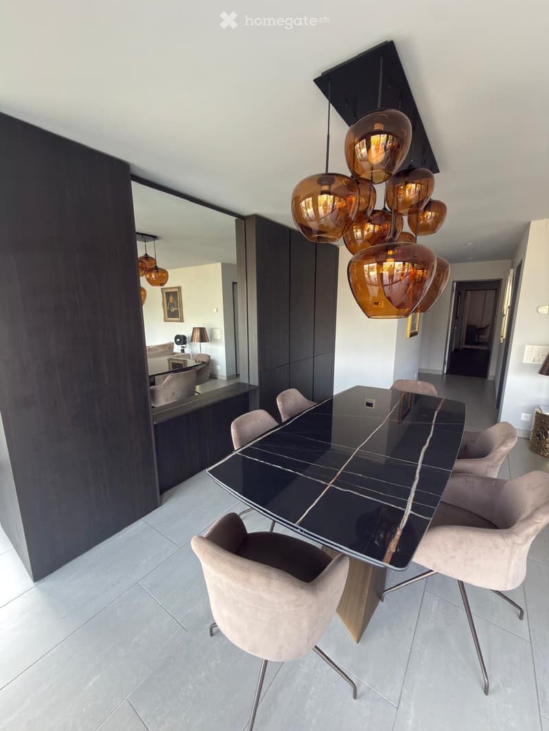 Modern dining area with a sleek black dining table, light-colored chairs, and a statement pendant light fixture.