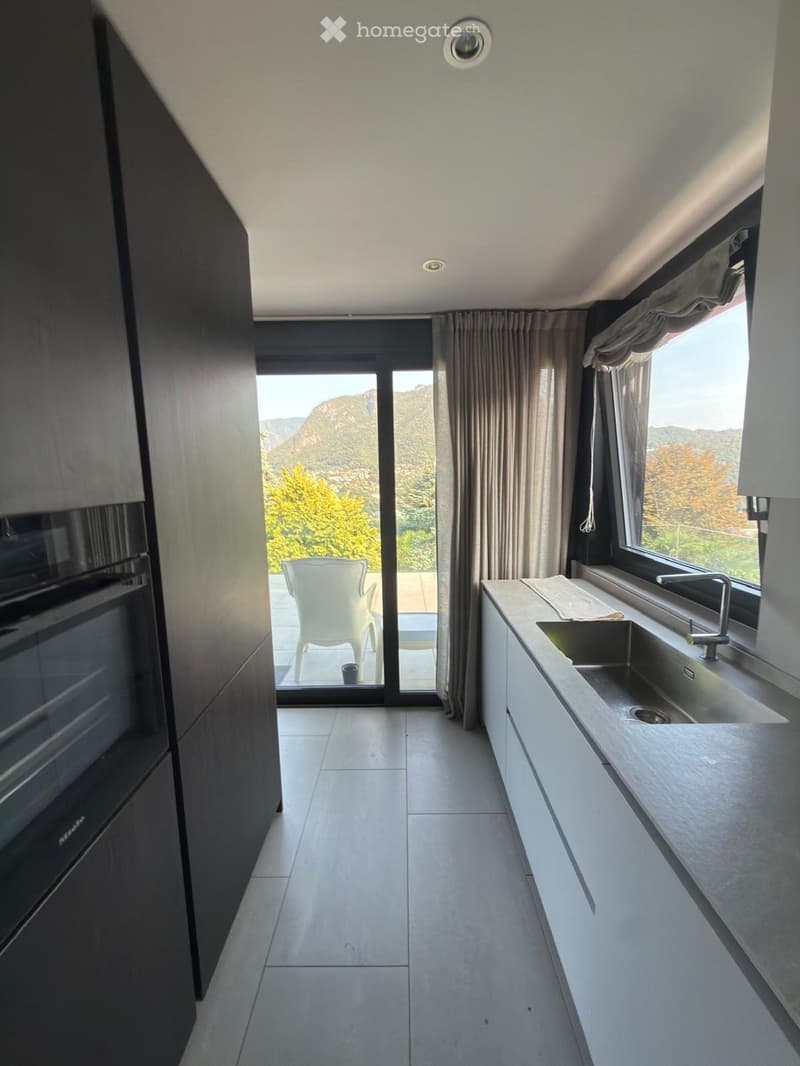 Modern kitchen with white cabinets, stainless steel sink, and a view of mountains through large windows and sliding doors.