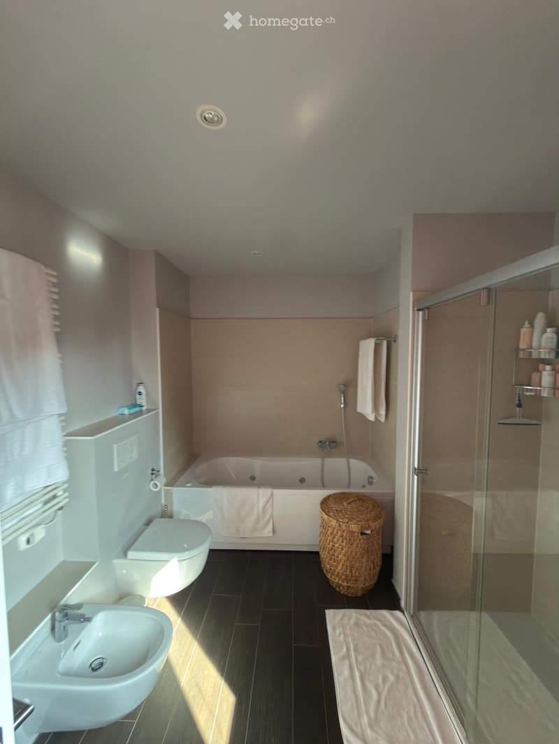 Modern bathroom with a bathtub, toilet, sink, wicker basket, and a glass-enclosed shower area with a shelf holding toiletries.