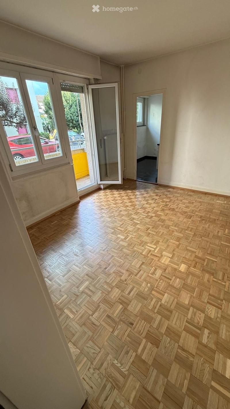 Empty room with wooden herringbone flooring, large windows, and an open door leading to a balcony.