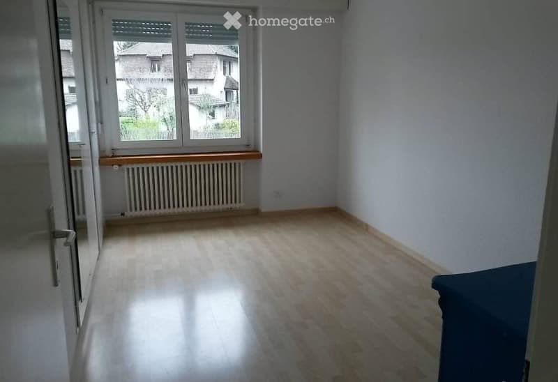 Empty room with light wooden flooring, white walls, and a large window with a radiator below it. No furniture or equipment is present.